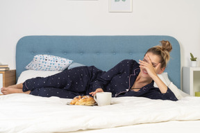 Front view of a laying in bed young lady having breakfast