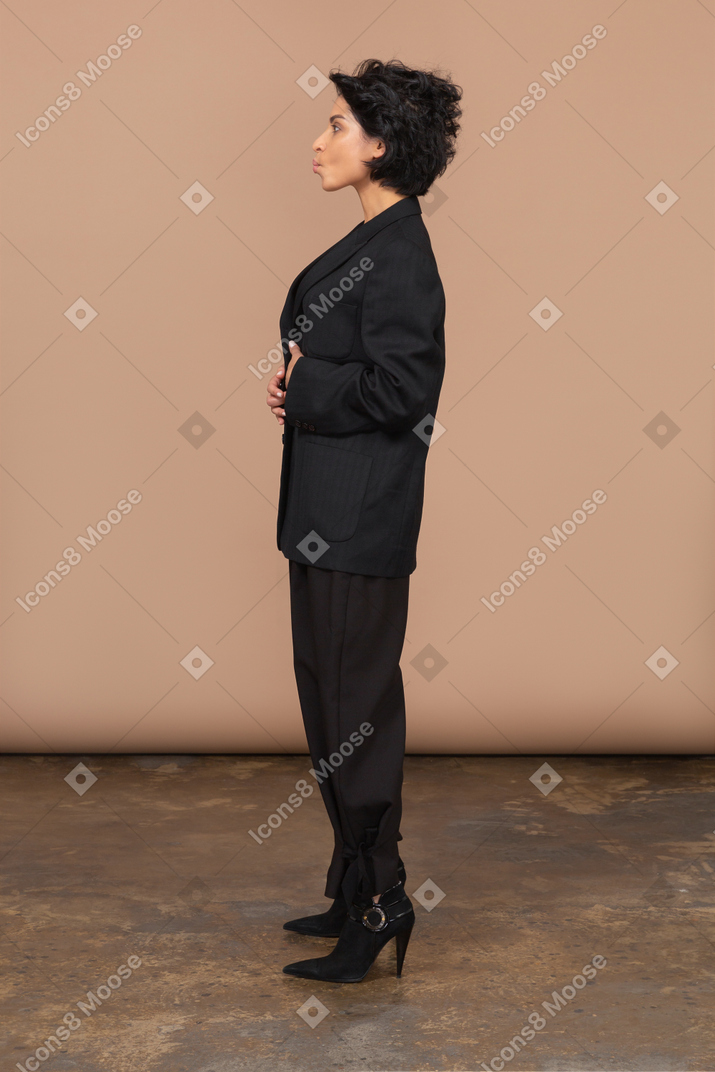 Side view of a businesswoman in a black suit putting hands on stomach and pouting