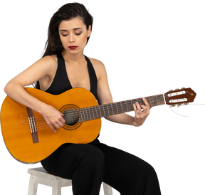 Vista frontal de uma jovem sentada de terno preto tocando violão