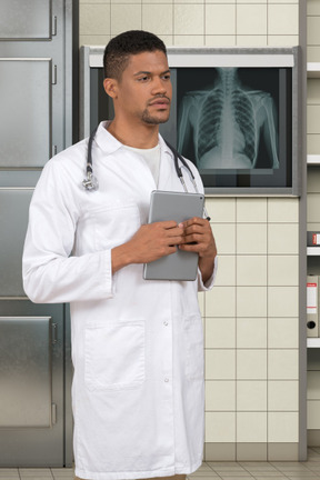 A male doctor in a white lab coat holding a tablet
