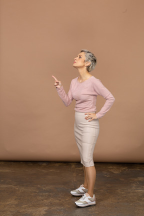 Vista lateral de una mujer en ropa casual apuntando hacia arriba con el dedo