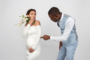 Groom pointing on his bride's belly while she's looking shocked