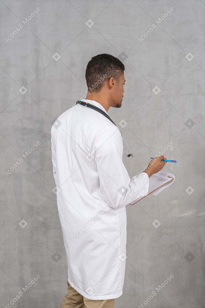 Vista posterior del médico varón tomando notas.