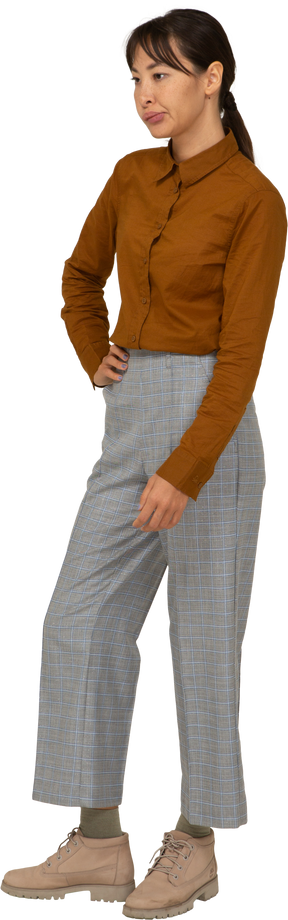 Vista de tres cuartos de una joven mujer asiática haciendo pucheros en calzones y blusa poniendo la mano en la cadera