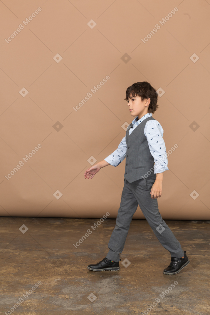 Vue latérale d'un garçon mignon en costume marchant