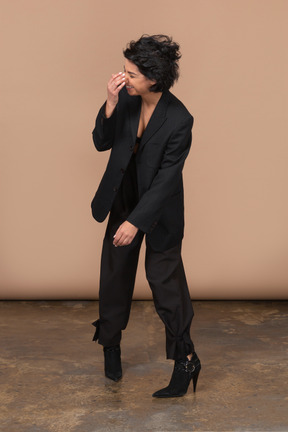 Vista frontal de una empresaria riendo vistiendo traje negro y tocando su nariz