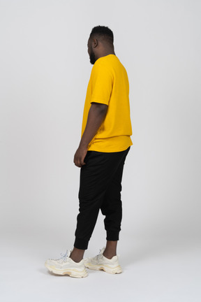 Three-quarter back view of a young dark-skinned man in yellow t-shirt standing still