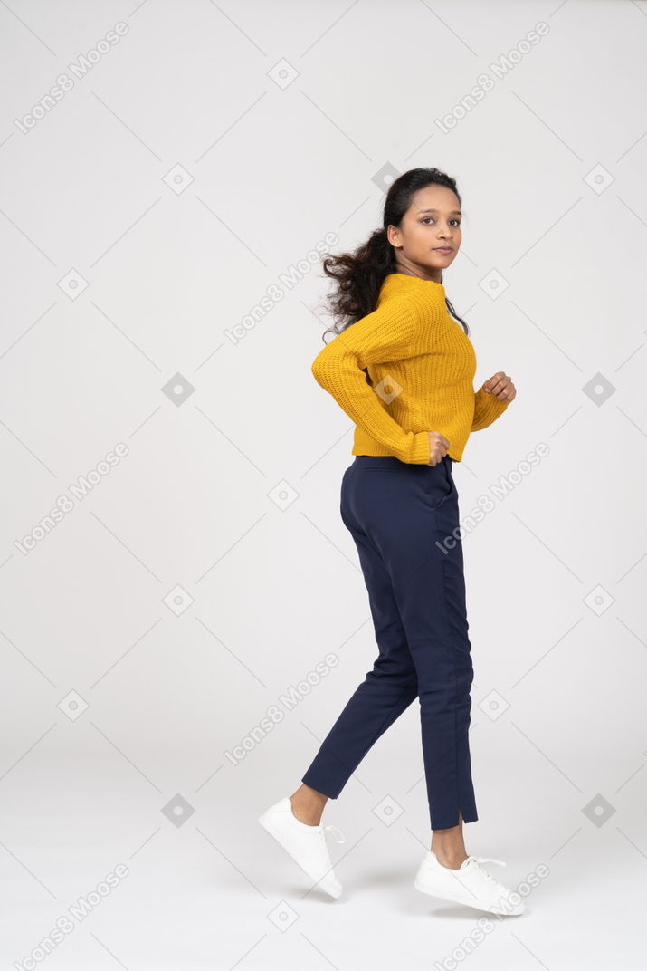 Side view of a girl in casual clothes running and looking at camera