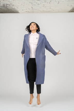 Excited woman in coat jumping and looking up