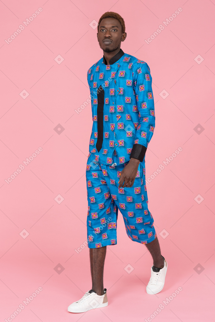 Homem negro de pijama azul andando sobre fundo rosa