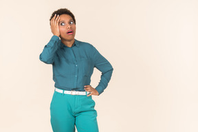 Mujer negra con un corte de pelo corto, vestida de azul, de pie contra un fondo pastel liso, con aspecto emocional