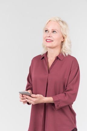 A nice-looking middle-aged blonde woman in a burgundy shirt and with a smartphone in her hand