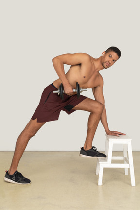 Side view of young man doing exercises with dumbbell