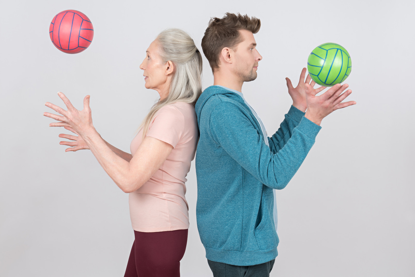 Old woman and young guy standing back to back and throwing colorful balls up