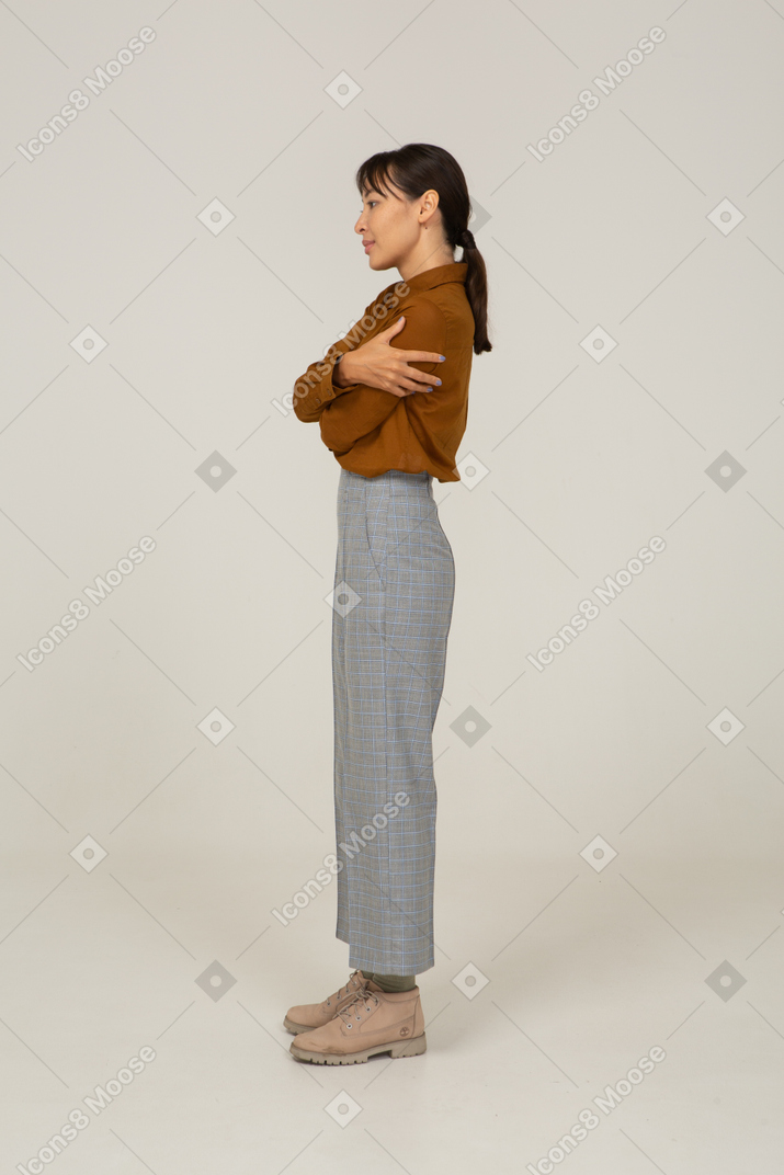 一位身着马裤和衬衫的年轻亚洲女性拥抱自己的侧视图