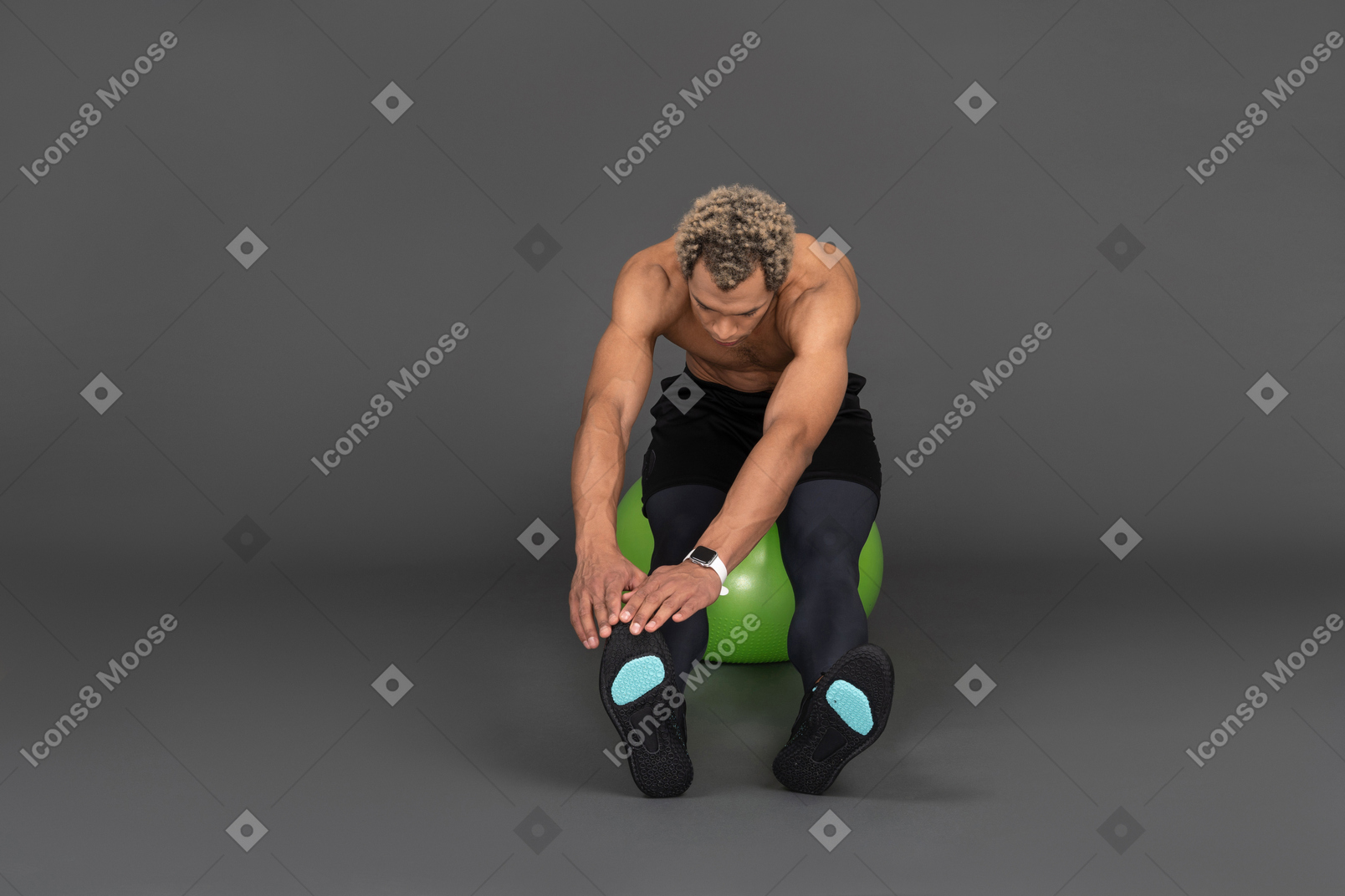Vista frontale di un uomo afro a torso nudo che si allunga mentre è seduto su una palla da palestra verde