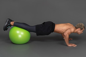 Seitenansicht eines hemdlosen afro-mannes, der liegestütze auf einem gymnastikball macht