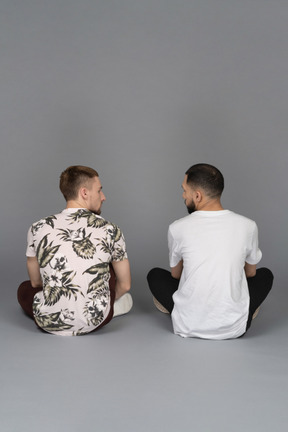 床に座ってお互いを見ている2人の若い男性の背面図