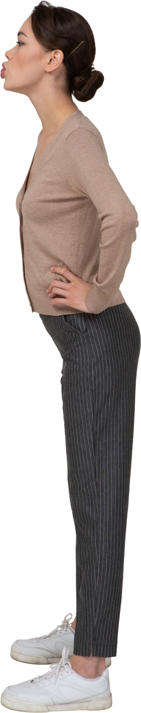 Vista laterale di una giovane donna in pullover e pantaloni inviando un bacio d'aria e mettendo le mani sui fianchi