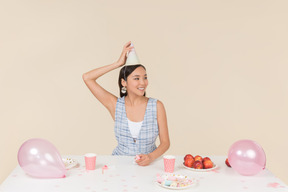 Joven asiática ajustando el cono de cumpleaños en la cabeza