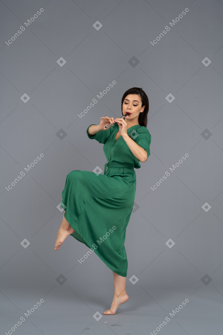Side view of a dancing young lady in green dress playing flute