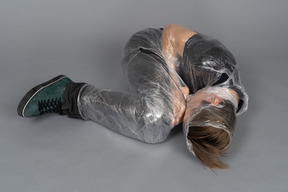 Young man lying down wrapped in plastic