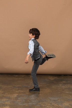 一个穿着灰色西装的男孩在一条腿上摆姿势的侧视图