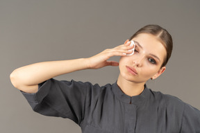 Vista frontal de una mujer joven en un mono quitando el maquillaje de ojos