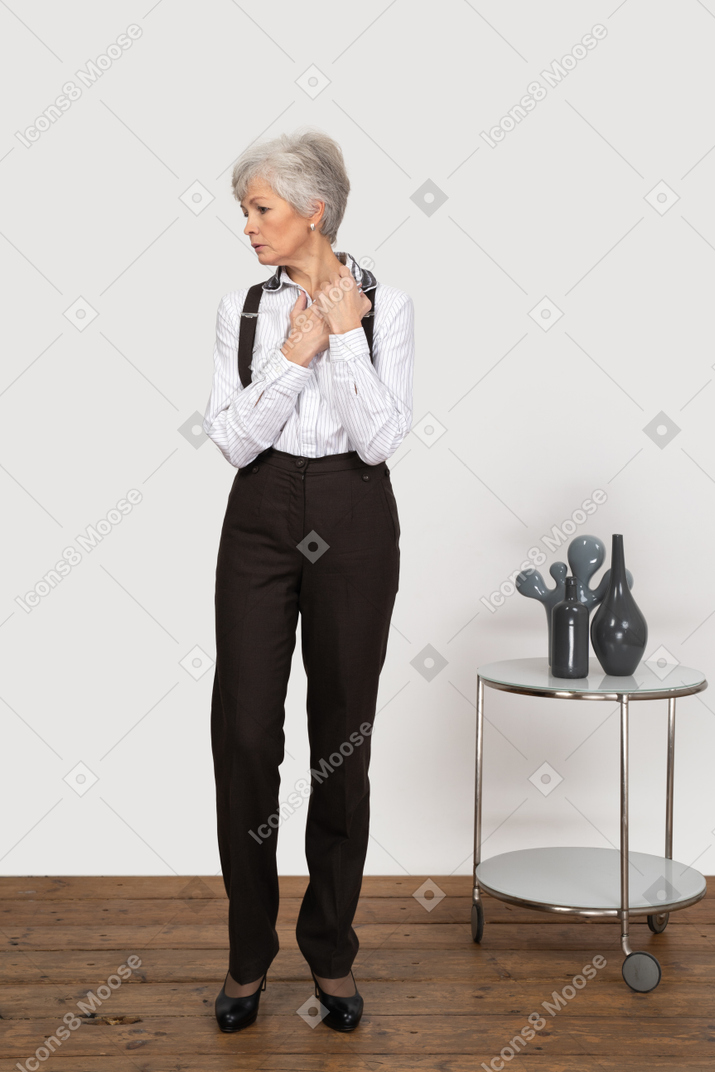 Front view of a worried old lady in office clothing holding hands together