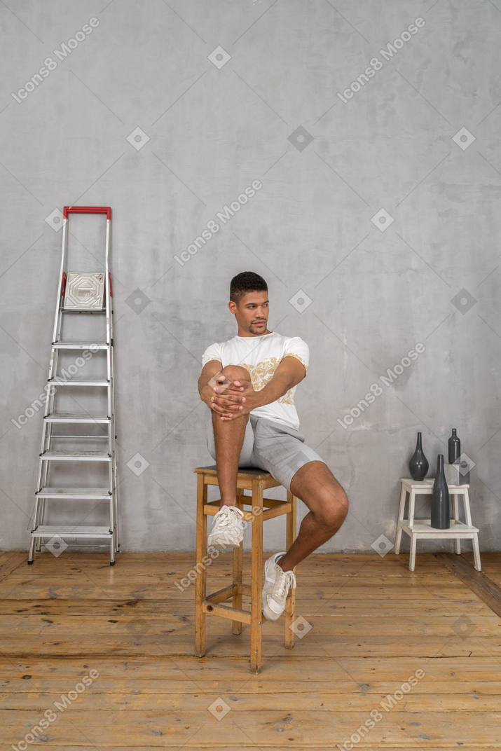 Мужчина сидит с руками на коленях и смотрит в сторону