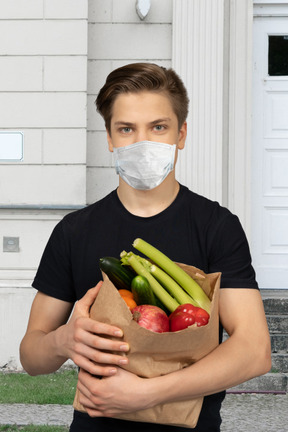 A man wearing a face mask holding a bag of vegetables