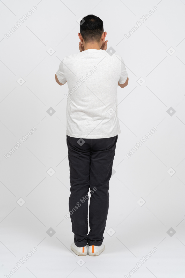 Мужчина в повседневной одежде стоит спиной к камере и закрывает лицо руками