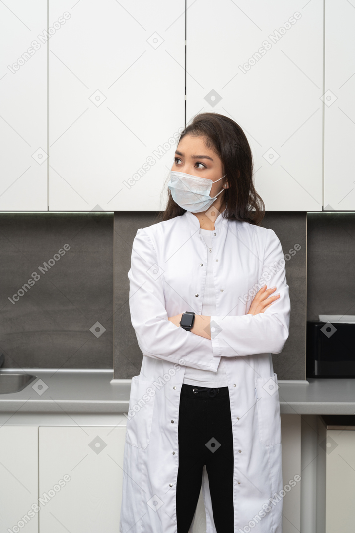 Front view of a doubtful female doctor crossing hands and looking up