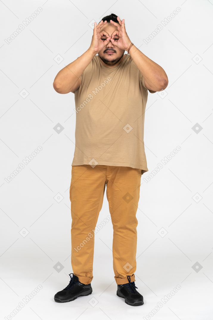 Funny asian man looking through his fingers imitating binoculars