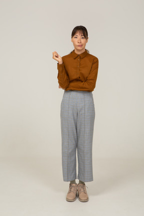 Vista frontal de uma jovem mulher asiática de calça e blusa, levantando a mão