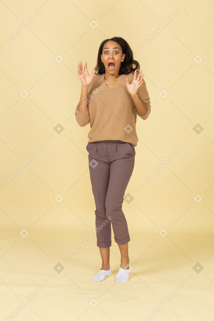 Вид в три четверти темнокожей испуганной молодой женщины, разводящей пальцы