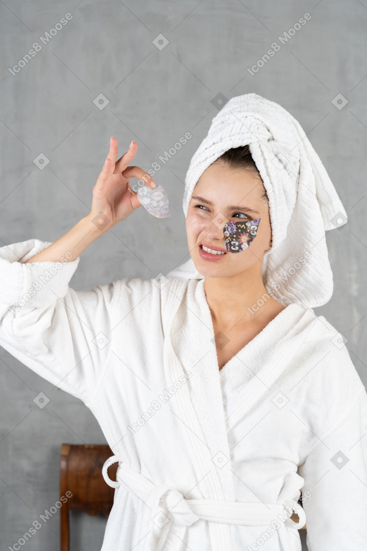 Woman in bathrobe peeling eye patch off