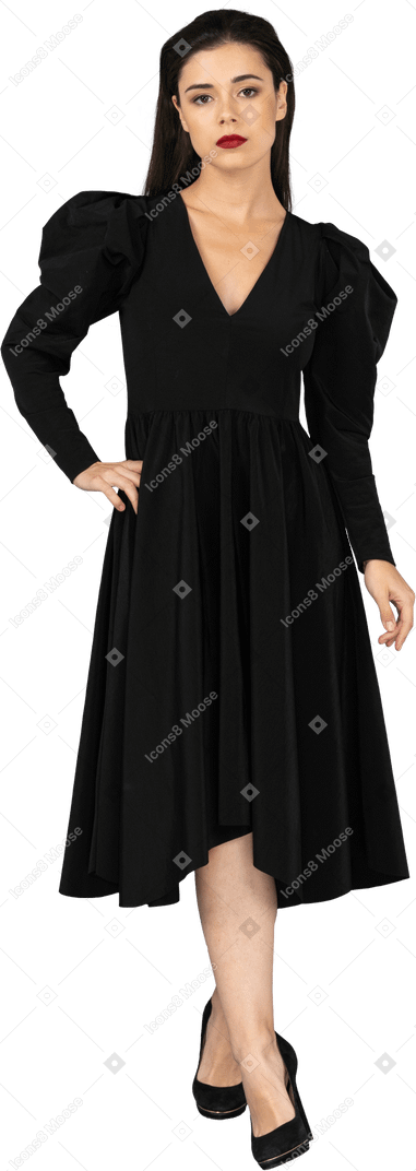 Vorderansicht einer jungen dame in einem schwarzen kleid, das hand auf hüfte legt