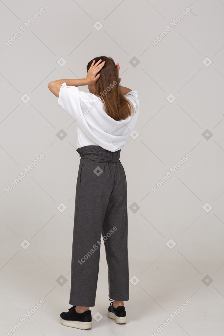 Back view of a young lady in office clothing touching her ears
