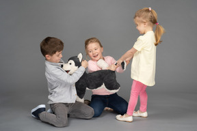 Three cute children playing with husky toy