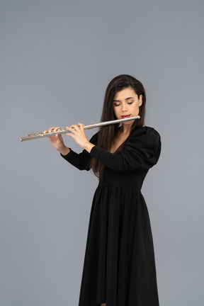 Front view of a serious young lady in black dress playing the flute