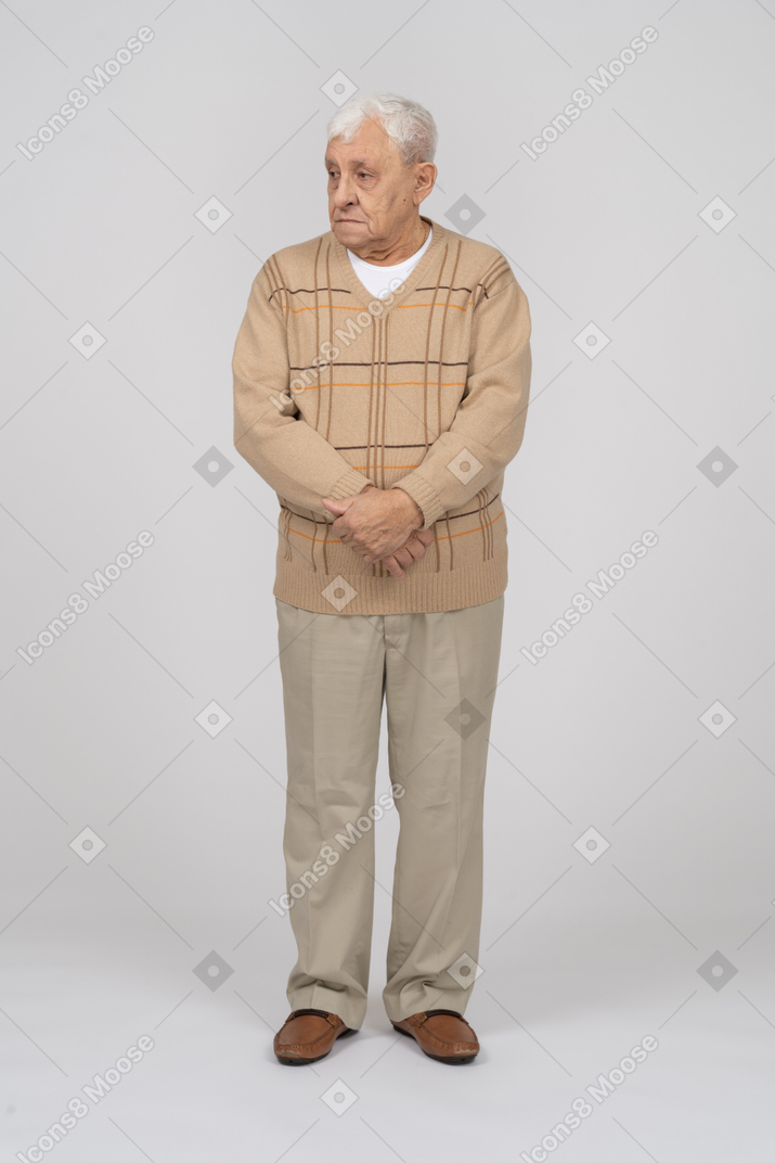 Front view of an old man in casual clothes standing with crossed hands and looking aside