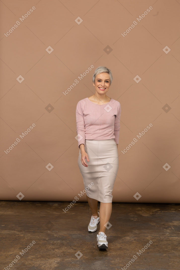 Vista frontal de una mujer feliz en ropa casual caminando hacia adelante