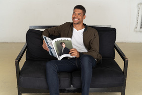 Beautiful young man sitting on a sofa and holding a magazine