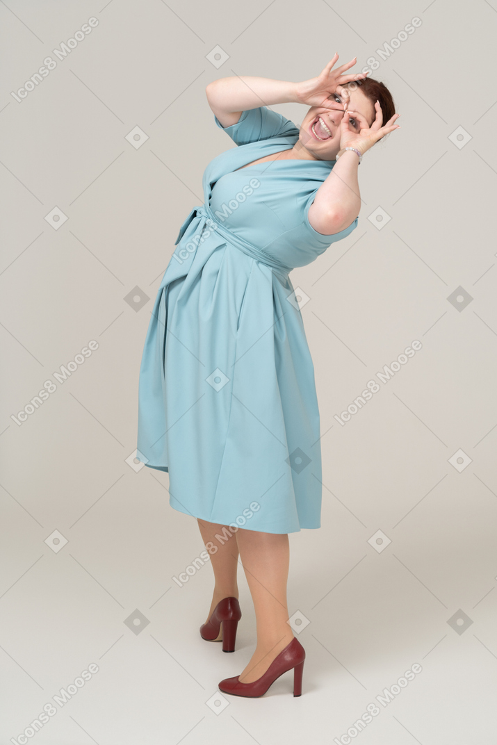 Вид сбоку на женщину в синем платье, смотрящую в воображаемый бинокль