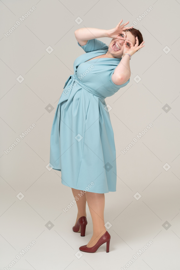 Side view of a woman in blue dress looking through imaginary binoculars