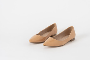 A three-quarter front shot of a pair of beige lacquer low heel shoes