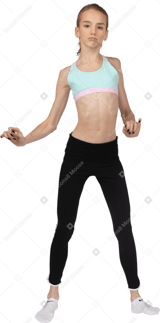 Front view of a teen girl in sportswear raising hands and her leg while dancing