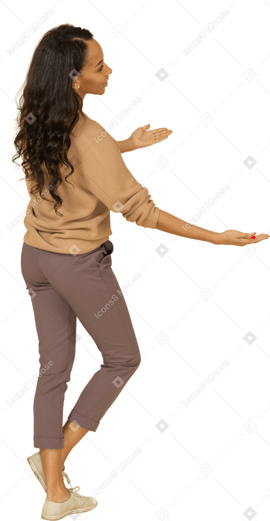 Vista posterior de tres cuartos de una mujer joven de piel oscura extendiendo sus manos