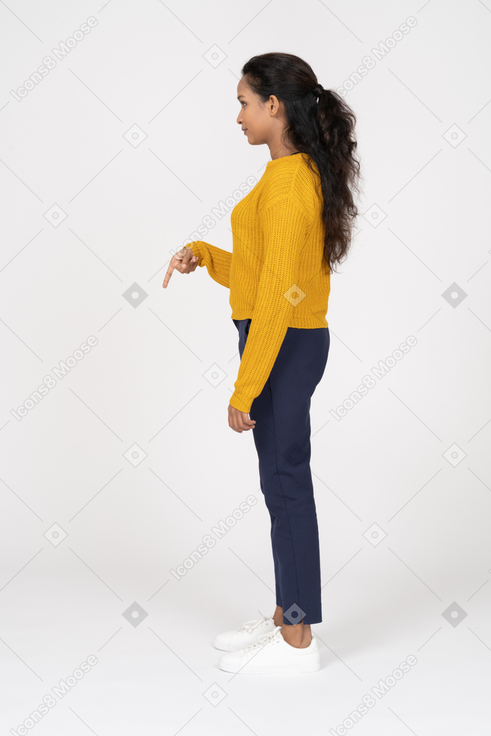 Vista lateral de una niña en ropa casual apuntando hacia abajo con un dedo
